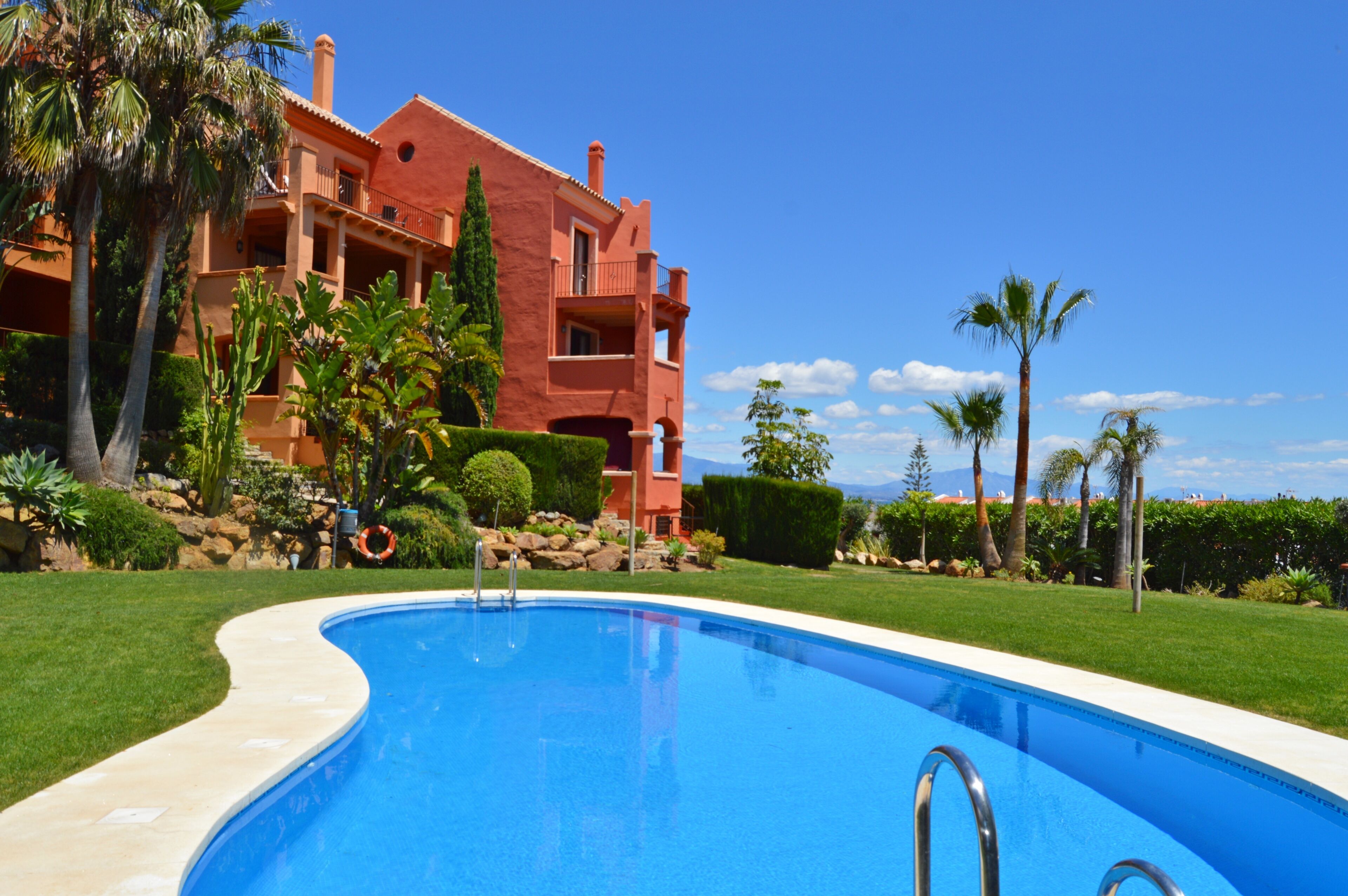 A swimming pool with a clear blue water, surrounded by a well-maintained lawn and palm trees.