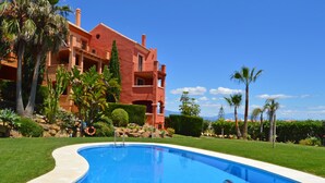 Una piscina con agua cristalina azul, rodeada de césped cuidado y palmeras.