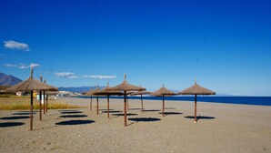 Una playa con varias sombrillas de paja y un cielo azul despejado.