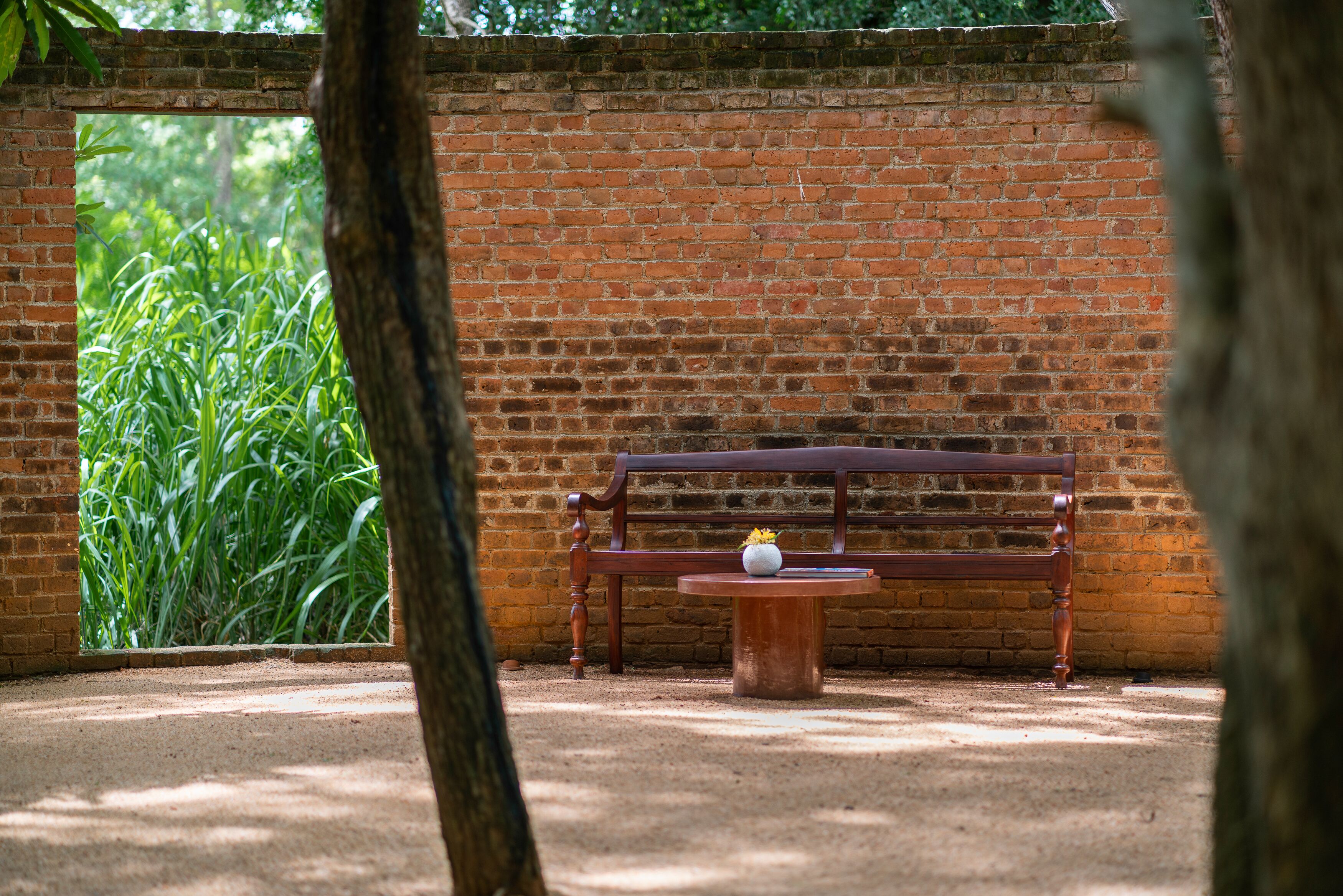 A brick wall with a bench and a small table with a vase.