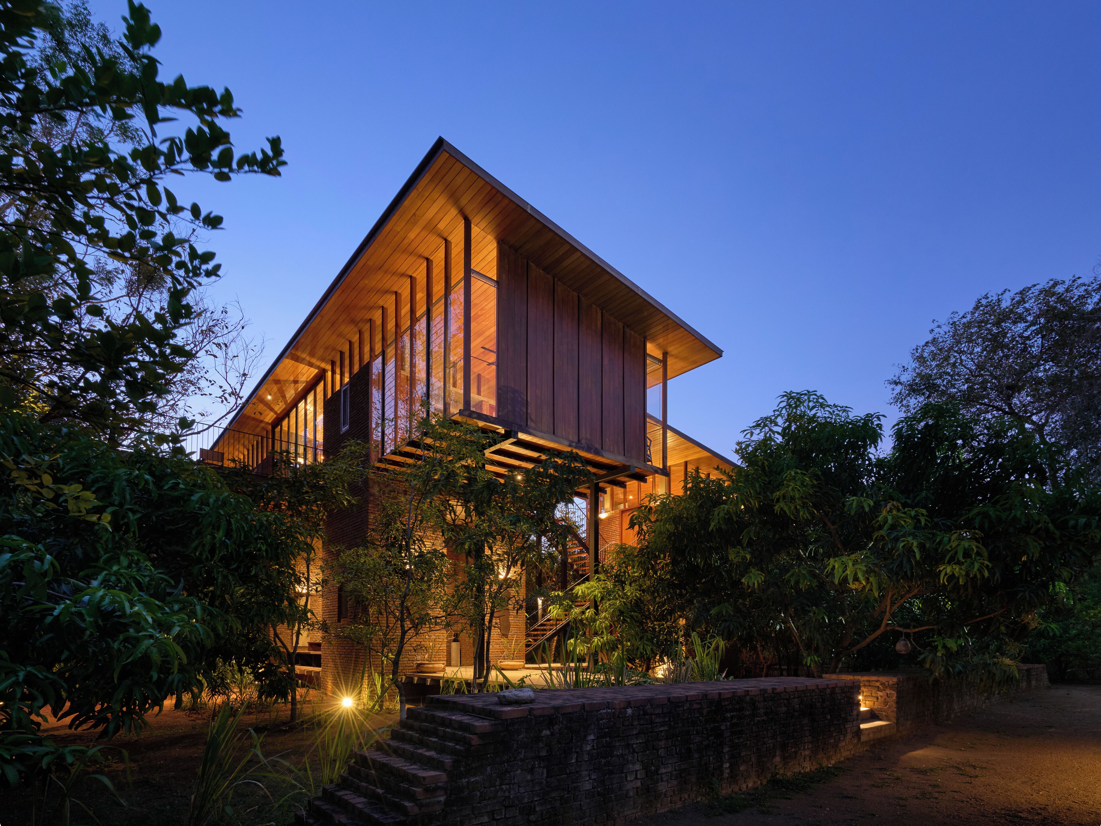 Une maison moderne, dotée d’une façade en bois et de grandes fenêtres, entourée d’une végétation luxuriante.
