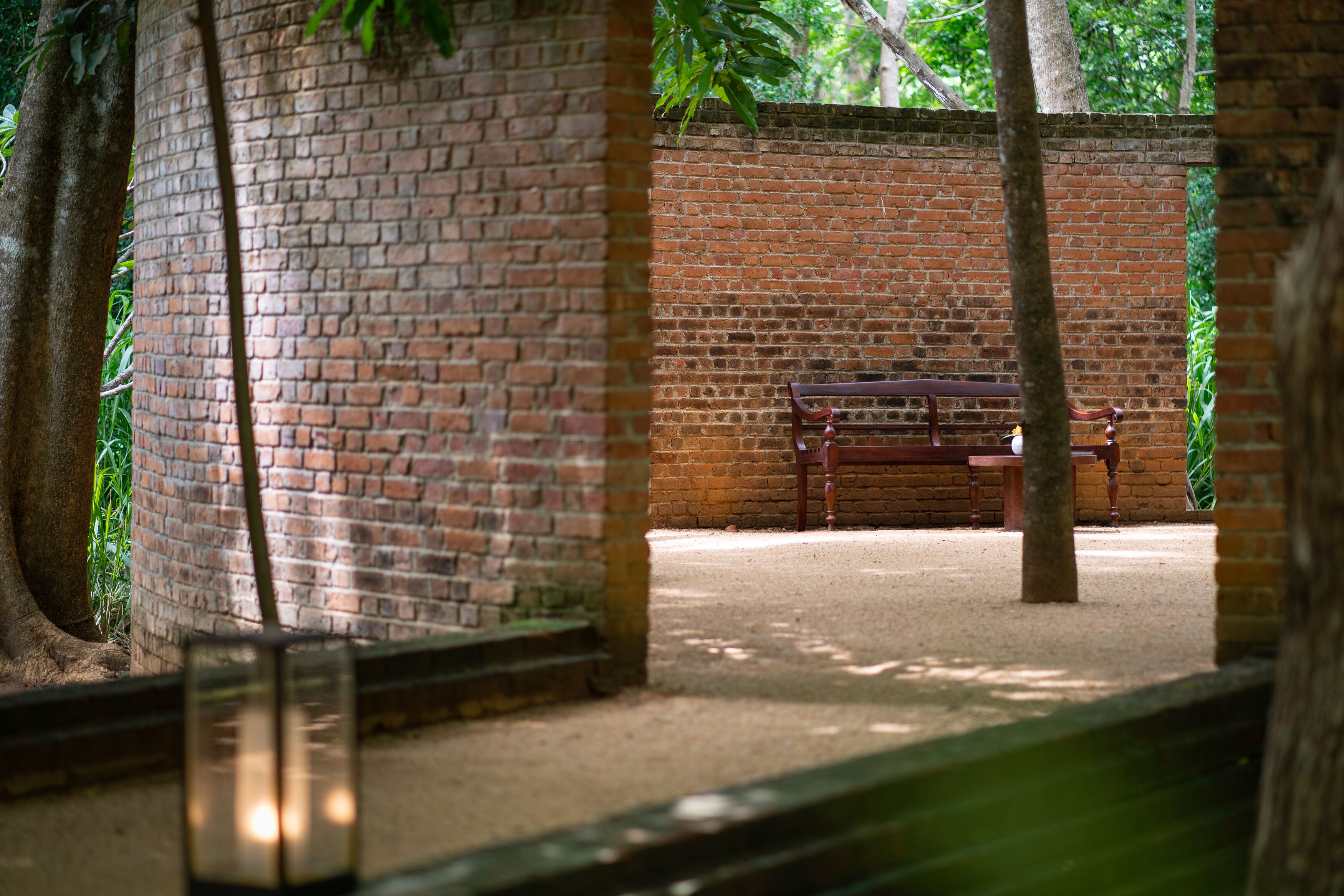 A brick wall with a bench and a tree in a shaded area.