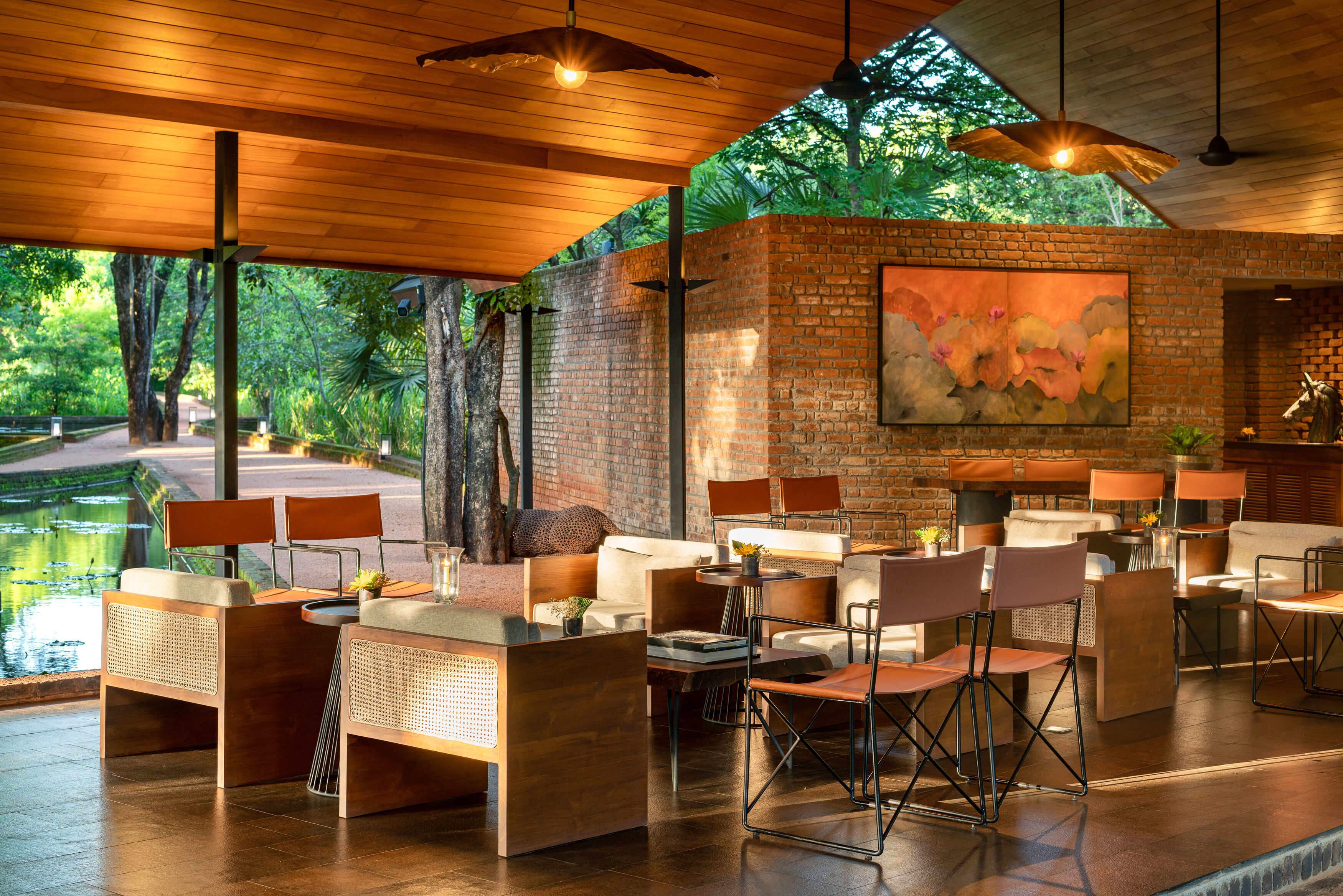 Un espacio moderno para comer al aire libre con paredes de ladrillo, techo de madera y vistas a un jardín.