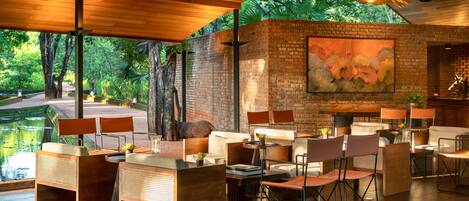 Un espacio moderno para comer al aire libre con paredes de ladrillo, techo de madera y vistas a un jardín.