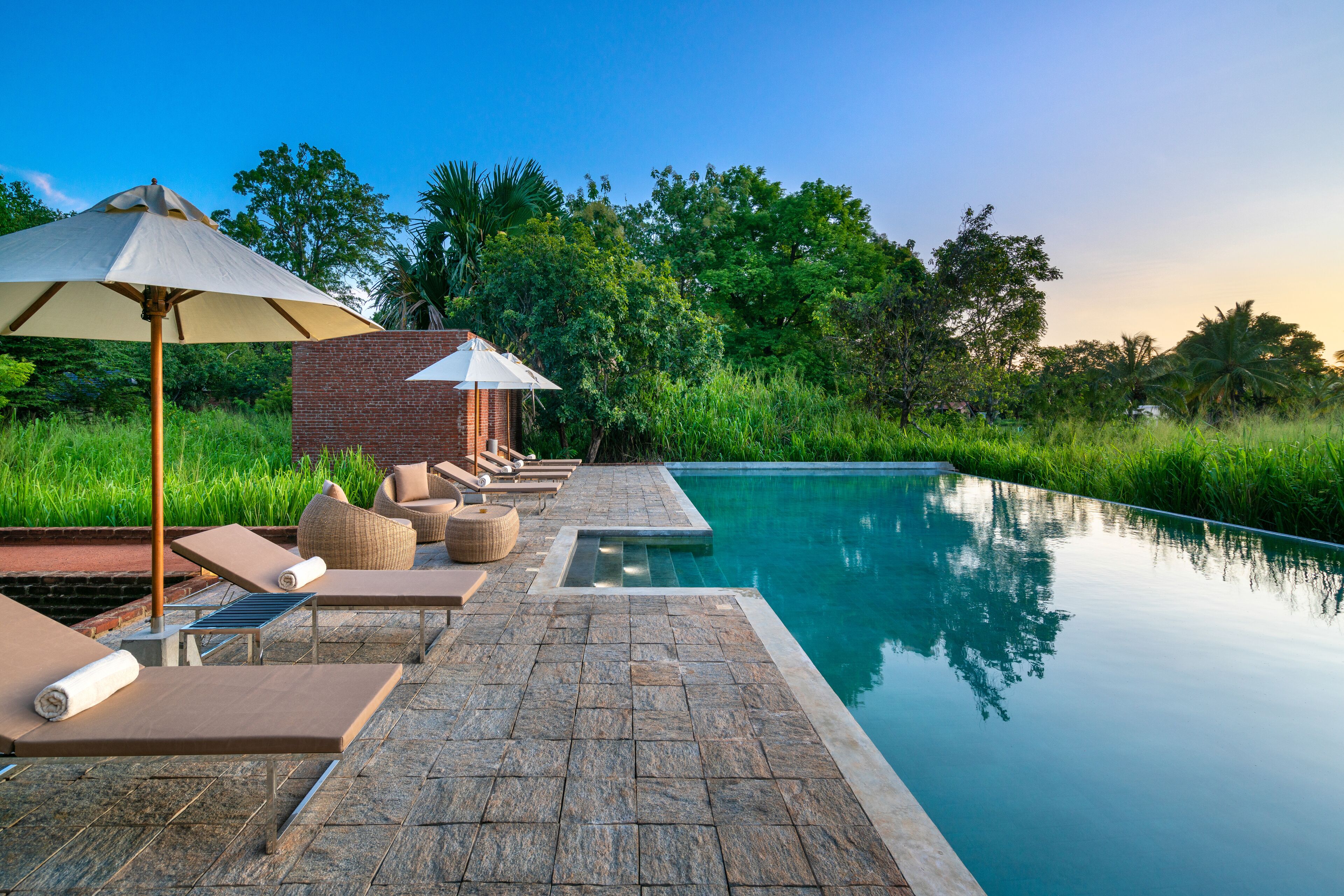 A serene infinity pool with lounge chairs and a brick structure in the background.
