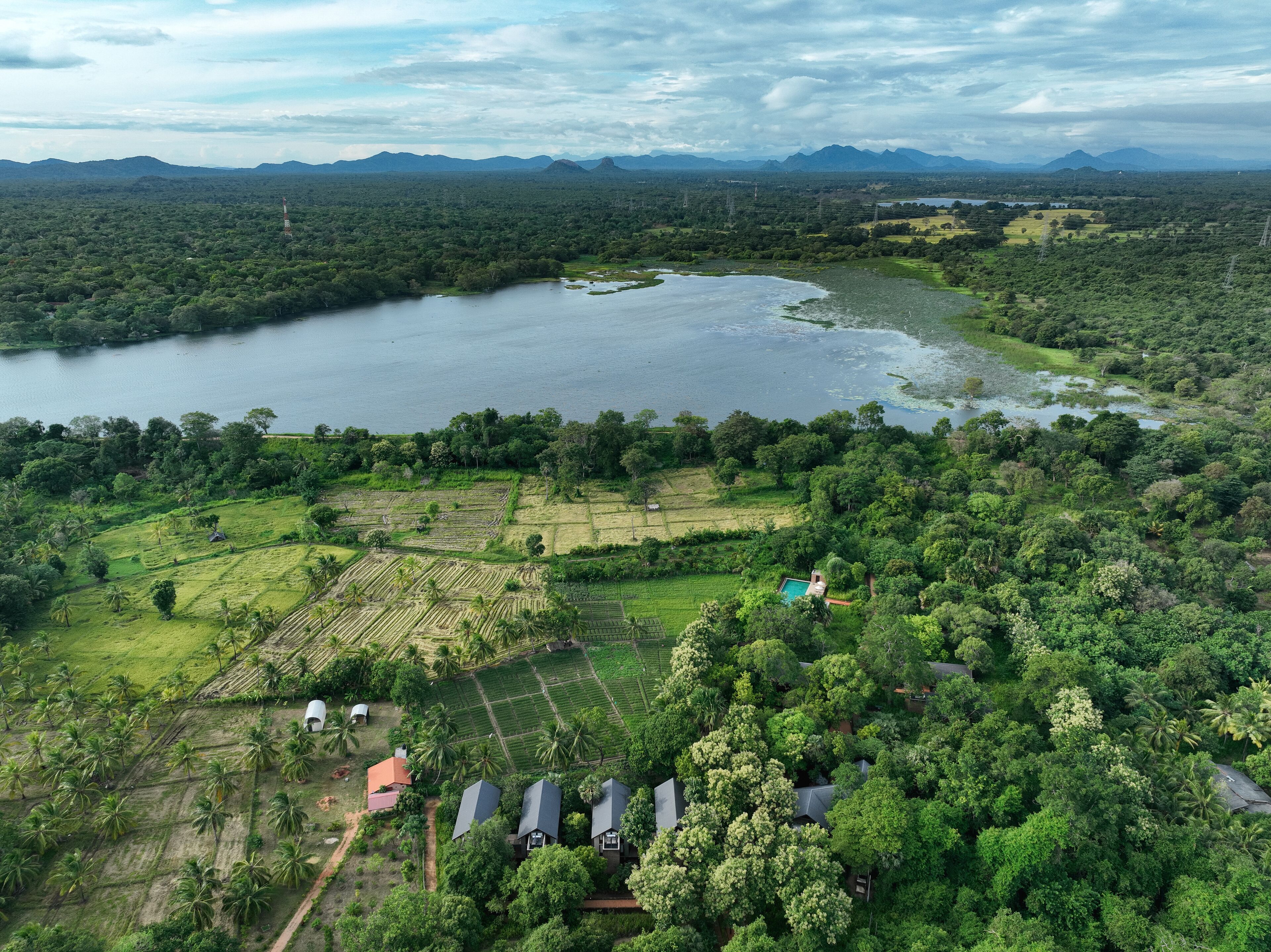 An aerial view of a tropical landscape with a large lake, surrounding greenery, and scattered houses.