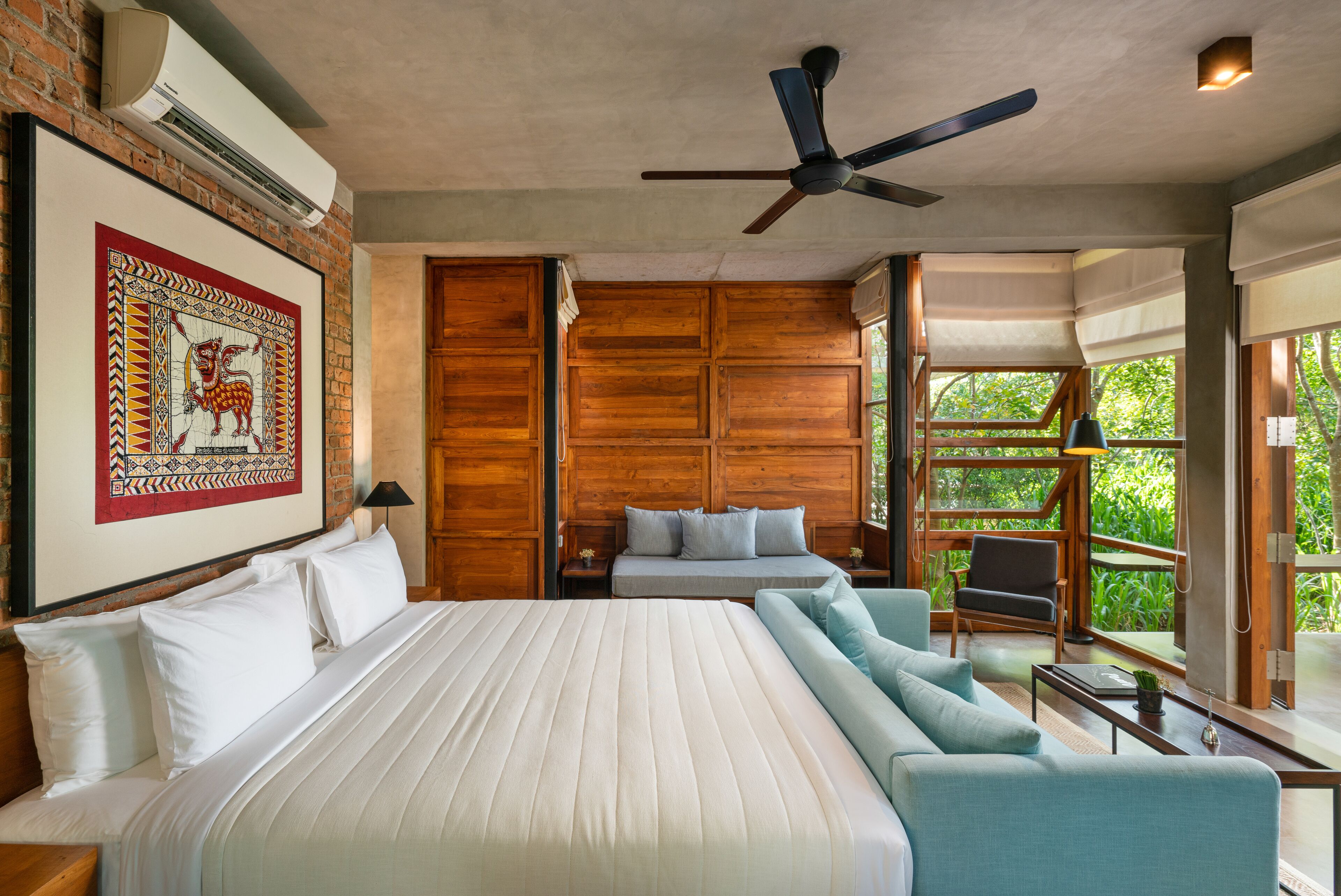 Un dormitorio con una cama grande, un sofá, un ventilador de techo y una ventana con vistas a zonas verdes.