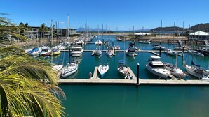 Ein Yachthafen mit mehreren Booten, die an Stegen liegen, umgeben von ruhigem Wasser und blauem Himmel.