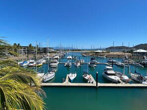 A marina with multiple boats docked at piers, surrounded by calm water and clear skies. - Blue on Blue Apartment 932 (Nelly Bay)
