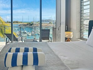A hotel room with a bed, a window with a view of a marina, and a chair by the window.