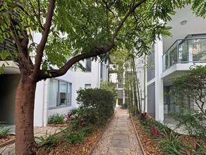 A pathway flanked by greenery and modern buildings with large windows. - Blue on Blue Apartment 932 (Nelly Bay)