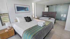 Ein modernes Hotelzimmer mit einem großen Bett, einem Badezimmer mit einer Glasdusche und Blick ins Freie.