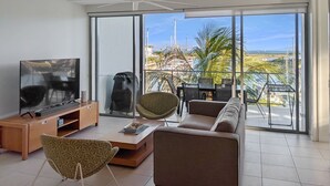 Ein modernes Wohnzimmer mit Fernseher, einer Couch, Sesseln und einem Balkon mit Blick auf den Yachthafen.