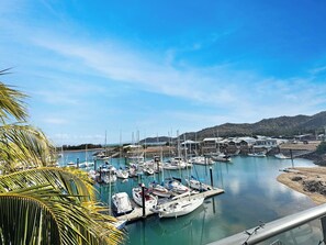 Un port de plaisance avec des bateaux amarrés, un ciel dégagé et un paysage vallonné en arrière-plan.