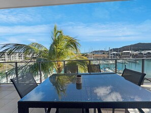 Une table entourée de chaises sur un balcon donnant sur une marina, avec des bateaux et un ciel dégagé.