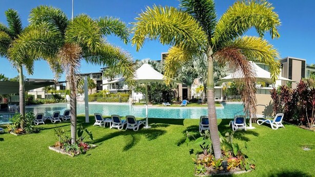 Ein Poolbereich mit Liegestühlen, Palmen und blauem Himmel.