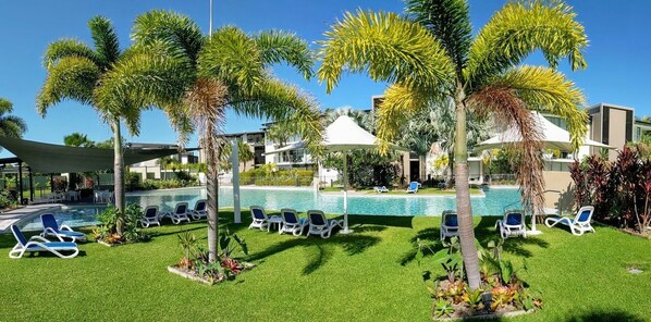 A pool area with lounge chairs, palm trees, and a clear sky. - Blue on Blue Apartment 932 (Nelly Bay)