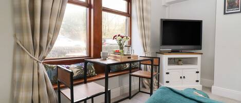 A cozy room with a window seat, a television, and a small table with a vase of flowers.