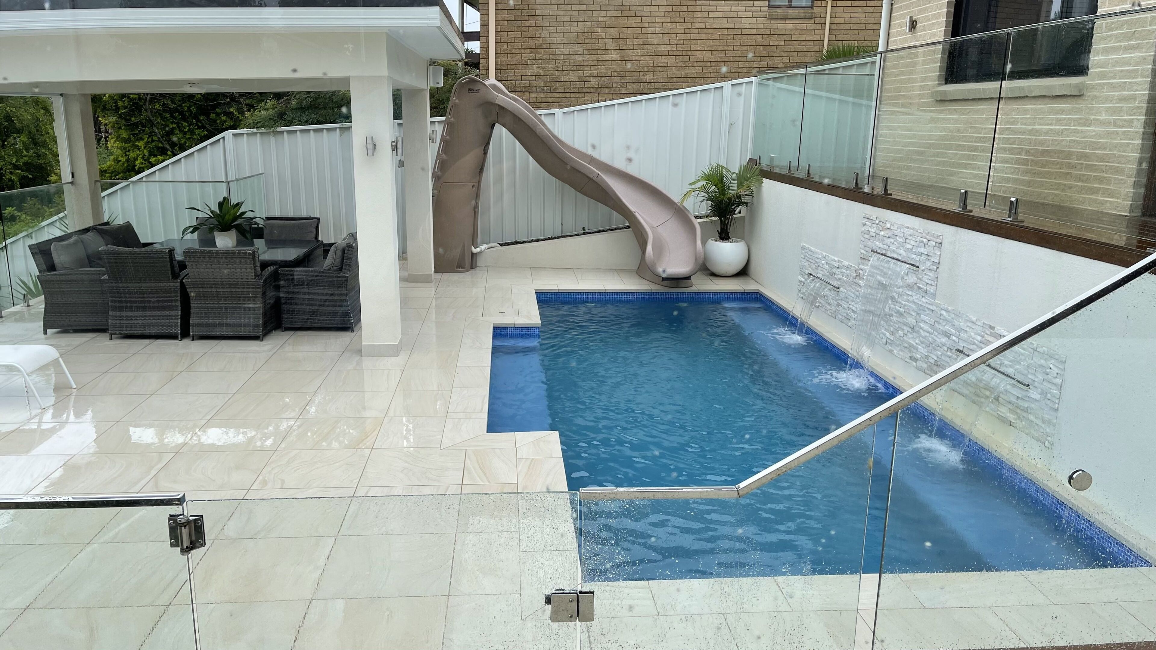 Une piscine avec un toboggan, du mobilier d’extérieur et un mur en briques.