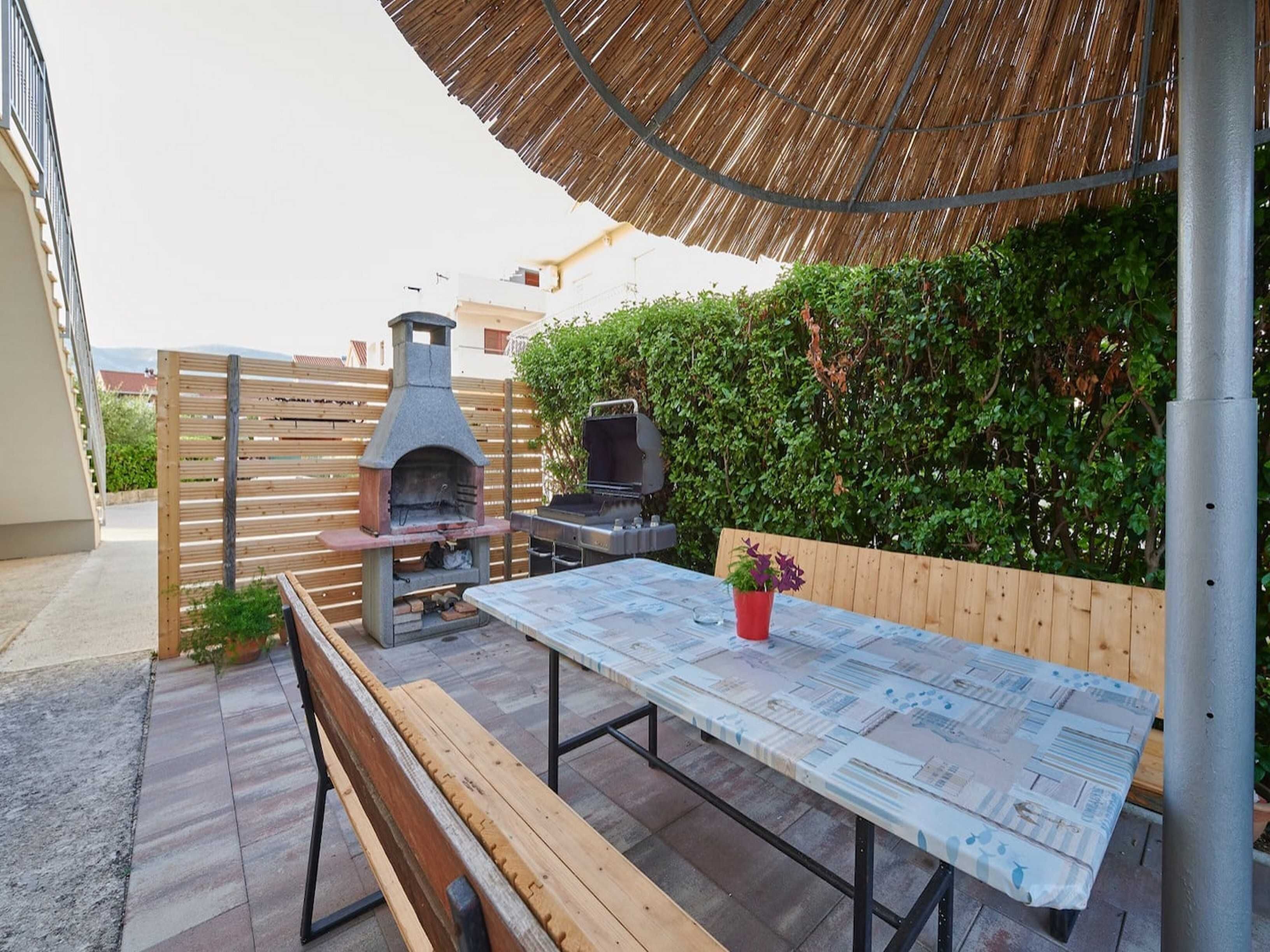 Un patio al aire libre con una mesa de madera, un banco, una parrilla y un horno de pizza.