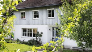 Ett tvåvåningshus med vit fasad, en synlig skorsten och en välskött gräsmatta.