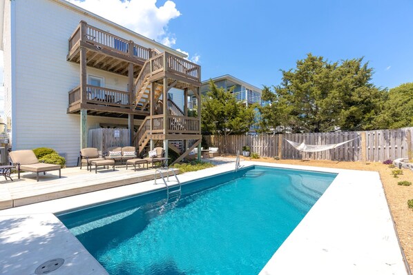 A swimming pool with a wooden deck and outdoor furniture.