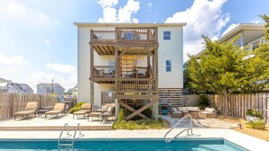 Ein zweistöckiges Gebäude mit Pool, Sitzgelegenheiten im Freien und einer Holzterrasse.