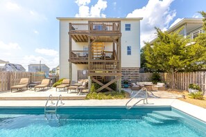 A two-story building with a pool, outdoor seating, and a wooden deck.