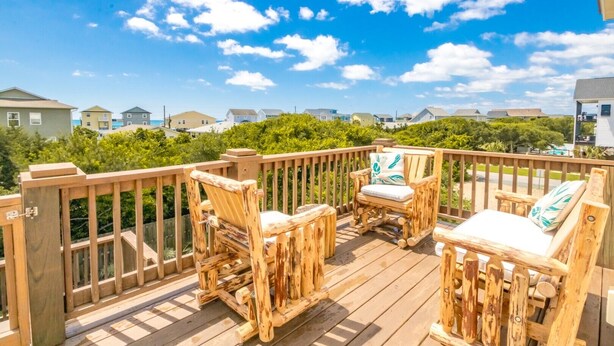 Une terrasse en bois, avec des meubles d’extérieur, une rambarde et une vue sur les maisons au loin.