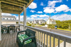 A covered porch with outdoor furniture, a view of a residential street, and houses in the background. - Sandy Bottoms - 4 Bedroom Home - Private Pool! (Surf City)