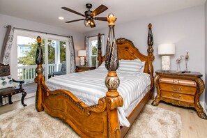A bedroom with a four-poster bed, a wooden nightstand, a dresser, and a ceiling fan.