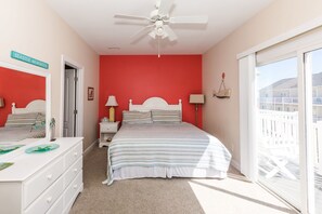 A bedroom with a bed, bedside tables, a dresser, a ceiling fan, and a window with a view of a balcony. - Sea-Esta! 4BR Townhome with Community Pool & easy beach access! (Surf City)