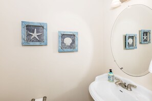 A bathroom with a sink, a mirror, and two wall-mounted decorative items. - Sea-Esta!  4BR Townhome with Community Pool & easy beach access! (Surf City)