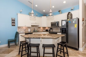A kitchen with white cabinets, a granite countertop, a black refrigerator, and three bar stools. - Sea-Esta! 4BR Townhome with Community Pool & easy beach access! (Surf City)