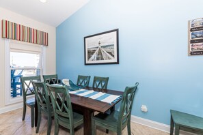 Een eethoek met een houten tafel, groene stoelen, een gestreept placemat en een lijst met een foto van een pier.