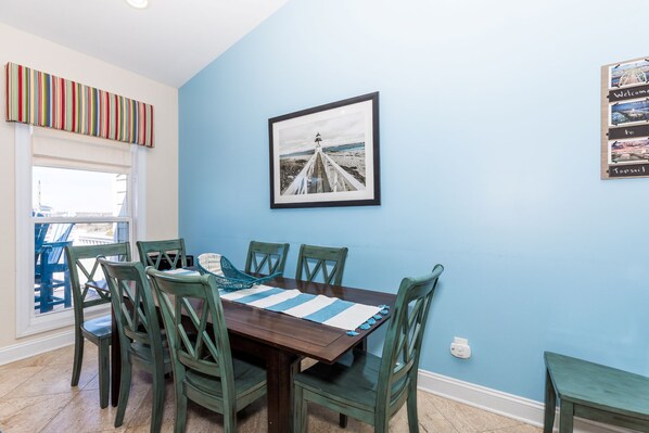 A dining area with a wooden table, green chairs, a striped placemat, and a framed picture of a pier. - Sea-Esta! 4BR Townhome with Community Pool & easy beach access! (Surf City)