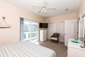 A bedroom with a bed, a dresser, a chair, a television, a ceiling fan, and a sliding glass door leading to a balcony. - Sea-Esta!  4BR Townhome with Community Pool & easy beach access! (Surf City)