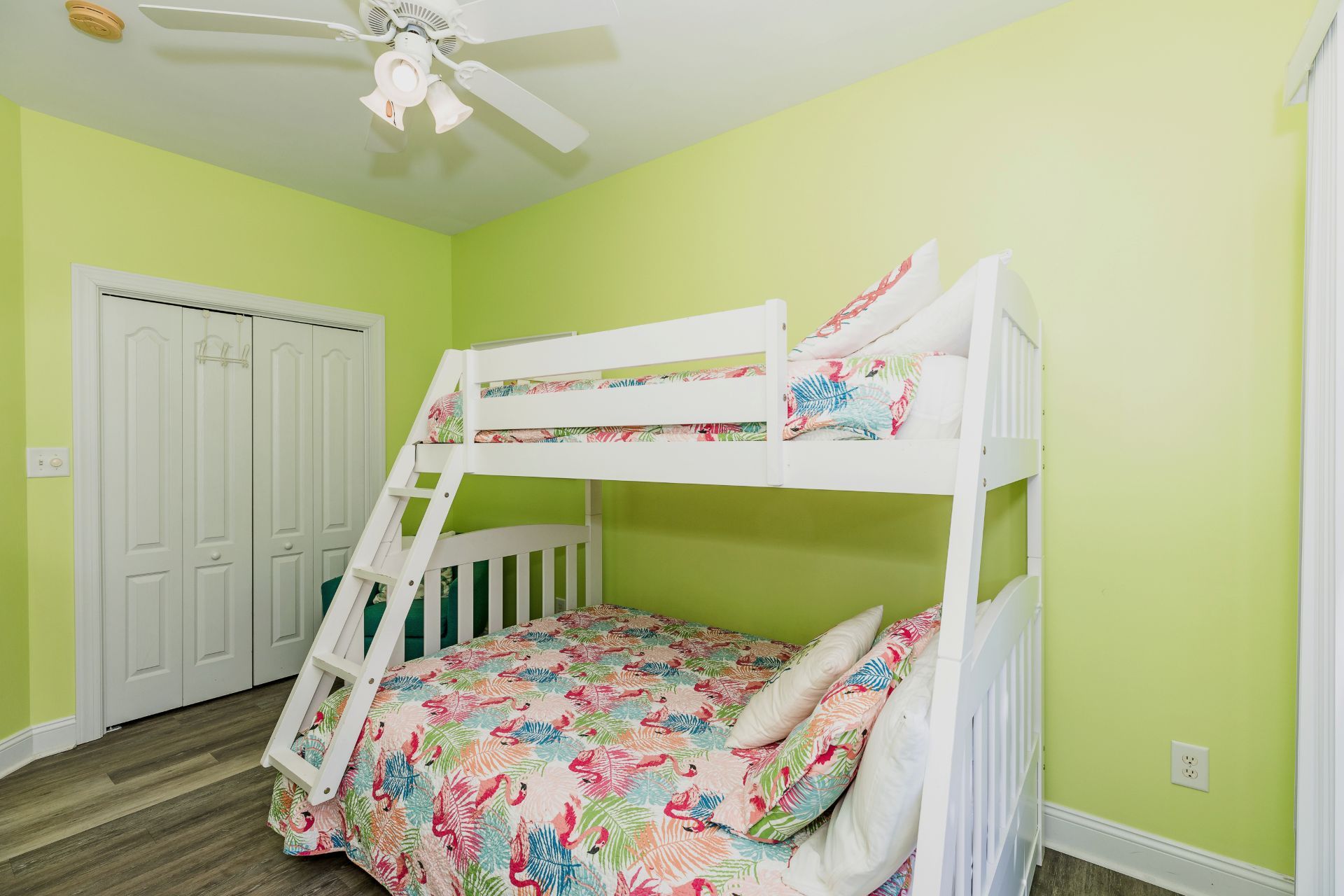 A bunk bed in a room with a ceiling fan, a door, and a light switch on the wall.