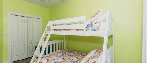 A bunk bed in a room with a ceiling fan, a door, and a light switch on the wall.