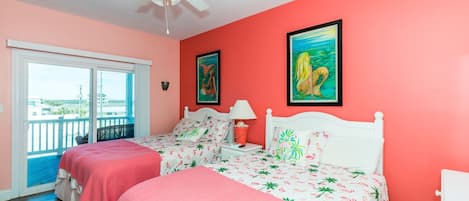 A room with two beds, a ceiling fan, a balcony with a view, and two framed paintings on the wall.
