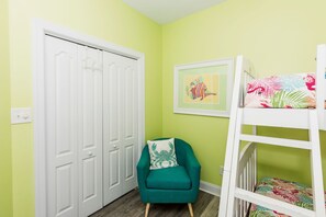 A room with a white door, a green armchair, a bunk bed with a colorful blanket, and a framed picture on the wall. - Sea-Esta! 4BR Townhome with Community Pool & easy beach access! (Surf City)