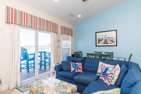 A living room with a blue sofa, a coffee table, and a view of the deck. - Sea-Esta! 4BR Townhome with Community Pool & easy beach access! (Surf City)