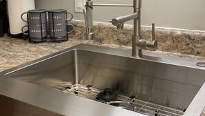 A stainless steel kitchen sink with a modern faucet, a granite countertop, and a wall-mounted utensil holder.