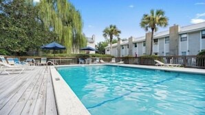 A swimming pool with a wooden deck, lounge chairs, and palm trees.