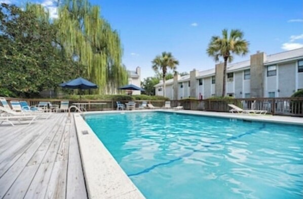 A swimming pool with a wooden deck, lounge chairs, and palm trees.
