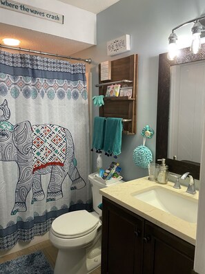A bathroom with a patterned shower curtain, a toilet, a sink with a mirror, and a towel rack. - NEWLY RENOVATED Island Condo- All new kitchen, floors, upgrades and appliances (St. Simons Island)