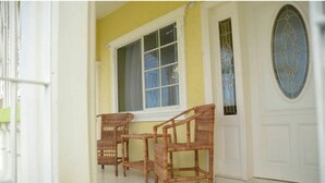 Eine gelbe Außenwand, eine weiße Tür mit Glasfenstern und drei Korbstühle davor.