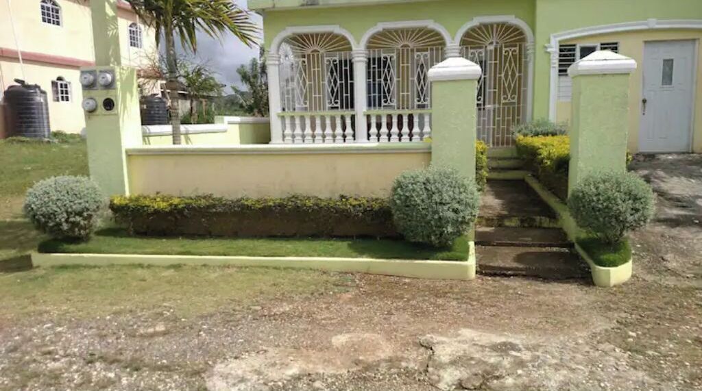 A two-story building with a green facade, a white balcony, and a gated entrance.