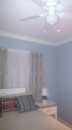 Une chambre à coucher avec un lit, une table de chevet, une lampe et un ventilateur de plafond.