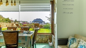 Un espace repas offrant une vue sur la mer, des sièges en plein air et un mur orné d’une citation inspirante.